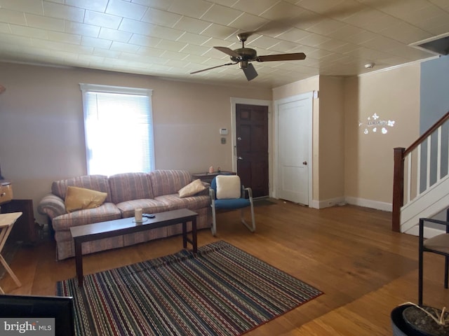 living area with stairway, a ceiling fan, baseboards, and wood finished floors