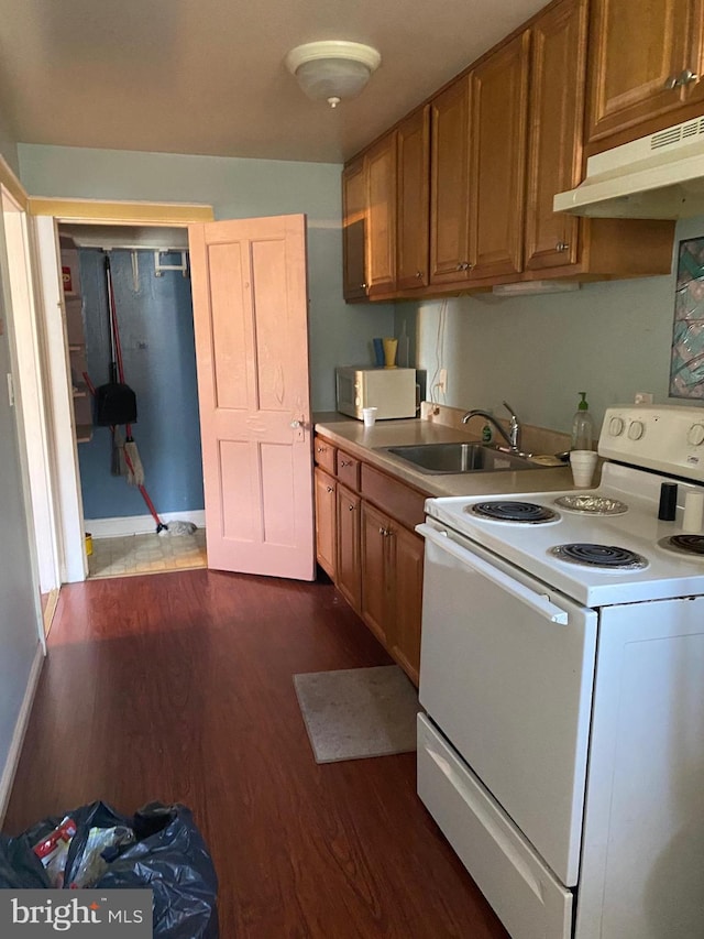 kitchen featuring dark wood-type flooring, white range with electric cooktop, under cabinet range hood, brown cabinetry, and a sink