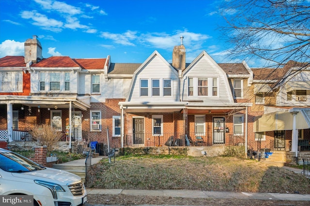 townhome / multi-family property featuring a gambrel roof, brick siding, a porch, and a chimney