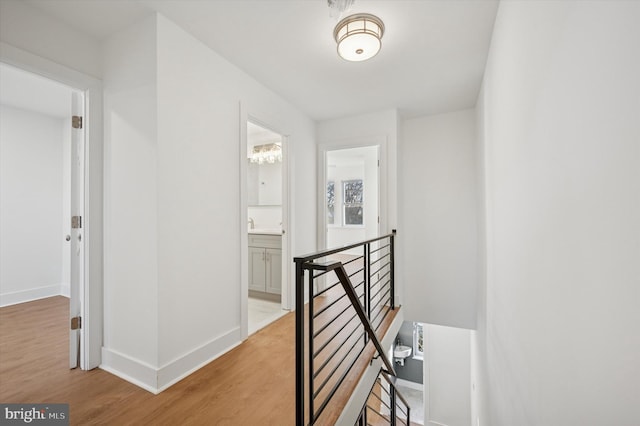 hall with wood finished floors, an upstairs landing, and baseboards