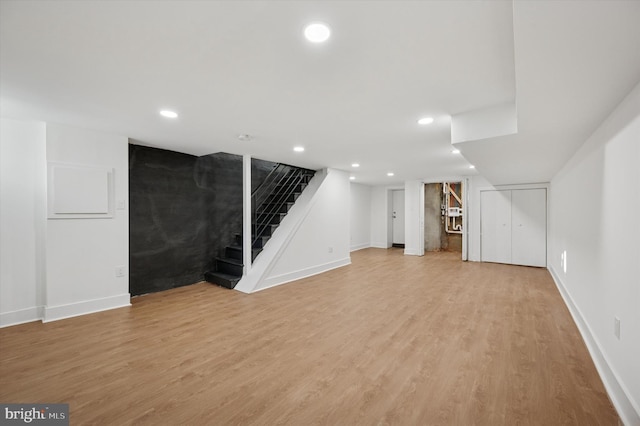 finished basement with stairs, light wood-style floors, and baseboards