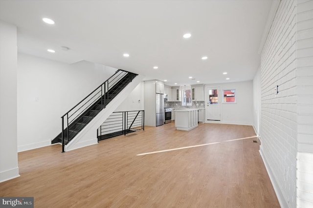 unfurnished living room featuring recessed lighting, baseboards, stairs, and light wood-style floors