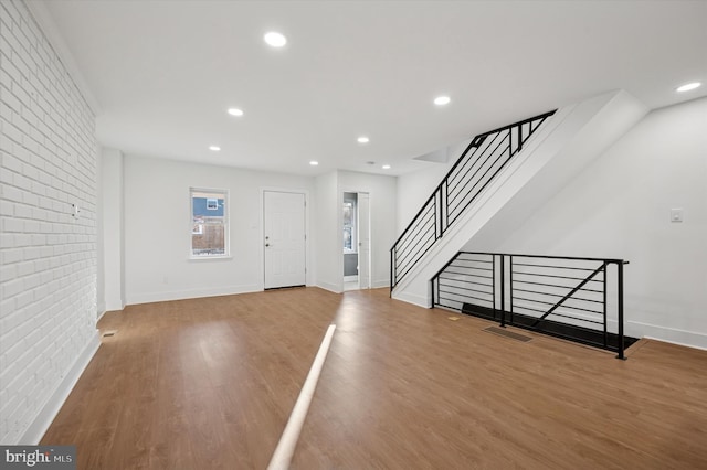 entryway featuring stairs, wood finished floors, baseboards, and brick wall