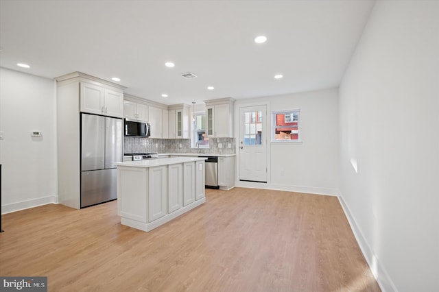 kitchen featuring backsplash, a kitchen island, light wood-type flooring, light countertops, and appliances with stainless steel finishes