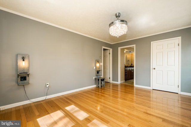 unfurnished bedroom featuring ornamental molding, connected bathroom, light wood-style floors, baseboards, and a chandelier