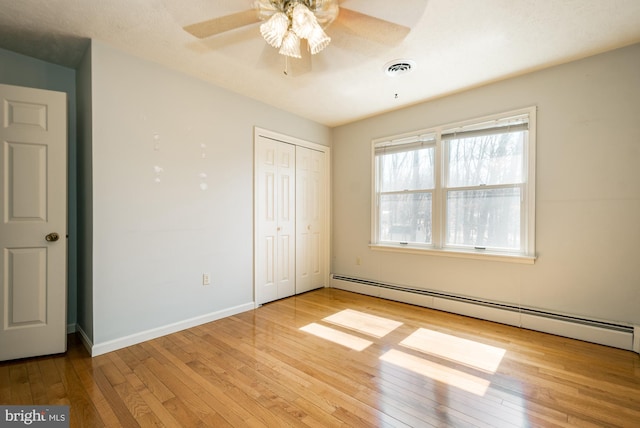 unfurnished bedroom featuring visible vents, a closet, wood-type flooring, a baseboard radiator, and baseboards