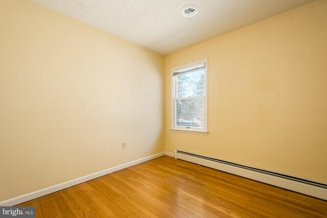 unfurnished room with a baseboard heating unit, visible vents, baseboards, and light wood-type flooring