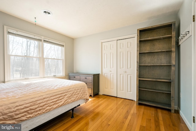 bedroom with light wood finished floors, visible vents, and a closet