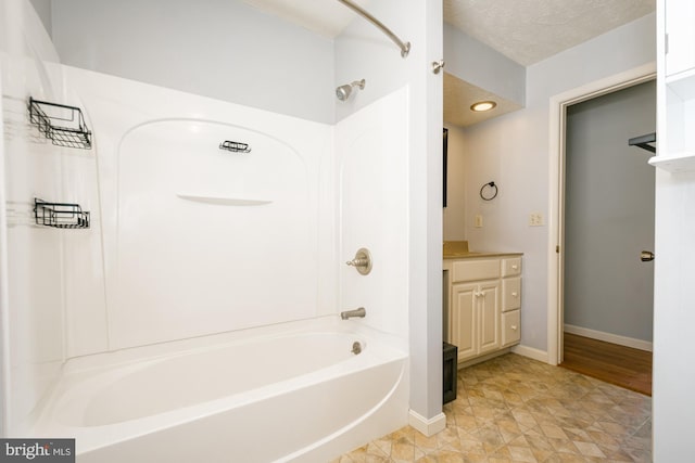 bathroom with baseboards, vanity, washtub / shower combination, and a textured ceiling