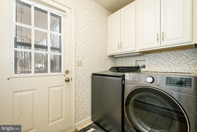 clothes washing area with wallpapered walls, washing machine and dryer, and cabinet space