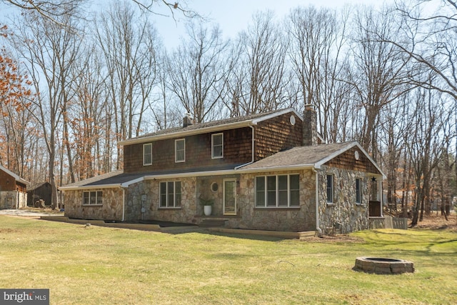 back of house with a yard, stone siding, a chimney, and an outdoor fire pit