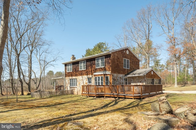 back of property with a wooden deck, a yard, stone siding, and a chimney