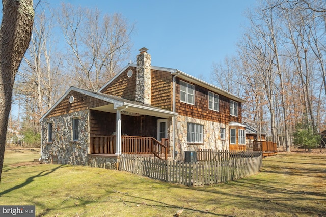 rear view of house featuring a yard, stone siding, a chimney, and fence