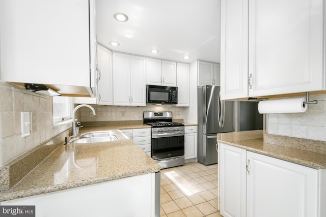 kitchen featuring a sink, white cabinetry, stainless steel appliances, decorative backsplash, and light stone countertops