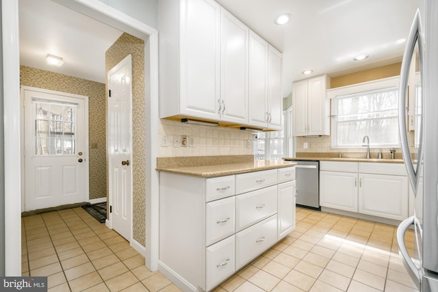 kitchen featuring wallpapered walls, a sink, white cabinetry, and stainless steel appliances