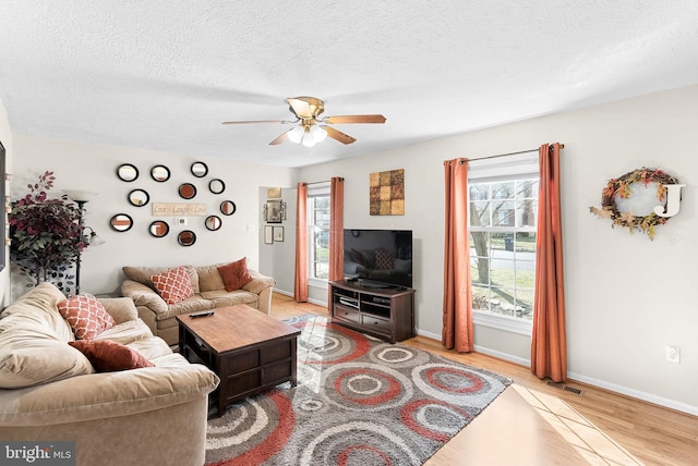 living area featuring visible vents, a ceiling fan, a textured ceiling, light wood finished floors, and baseboards