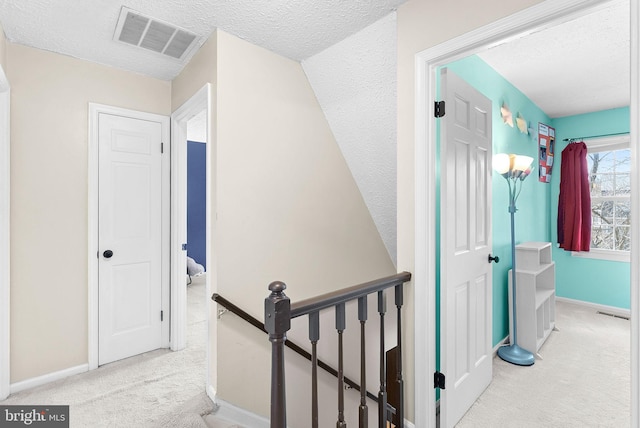 corridor with carpet, visible vents, baseboards, a textured ceiling, and an upstairs landing