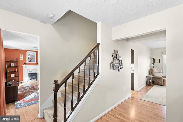 staircase featuring a fireplace, wood finished floors, baseboards, and a textured ceiling