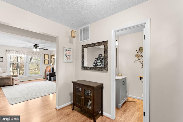 corridor featuring visible vents, baseboards, a textured ceiling, and light wood-style flooring