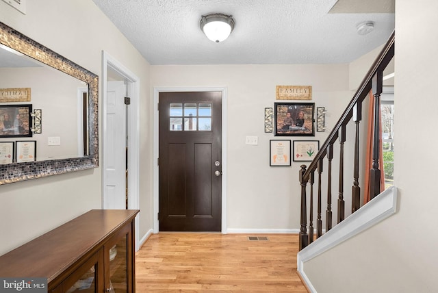 foyer featuring stairway, baseboards, light wood-style floors, and visible vents