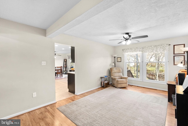 living area featuring baseboards, a textured ceiling, light wood-type flooring, and a ceiling fan