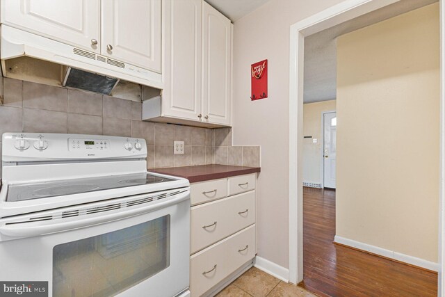 kitchen with baseboards, decorative backsplash, electric stove, under cabinet range hood, and white cabinetry