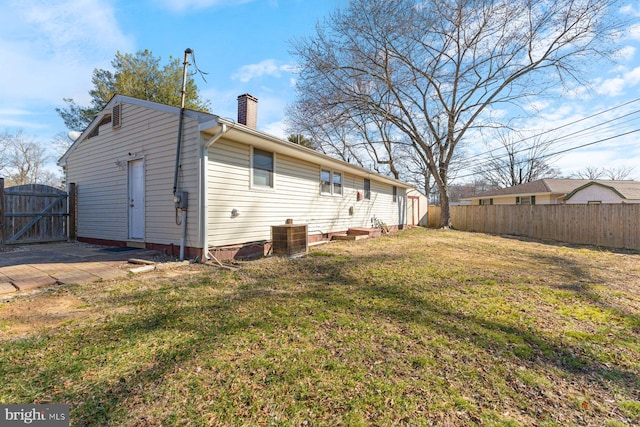 rear view of property featuring fence, central AC, a lawn, a chimney, and a gate