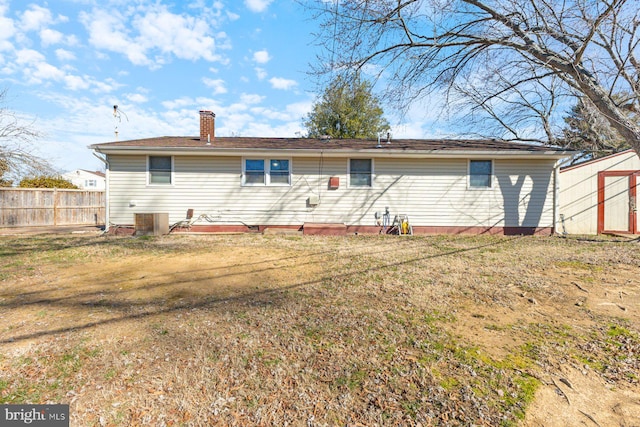 rear view of house with cooling unit, fence, a lawn, and a chimney