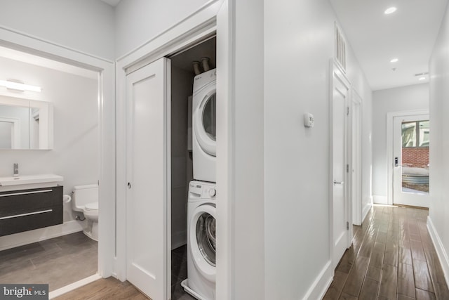 clothes washing area with dark wood-type flooring, baseboards, stacked washer and dryer, laundry area, and recessed lighting