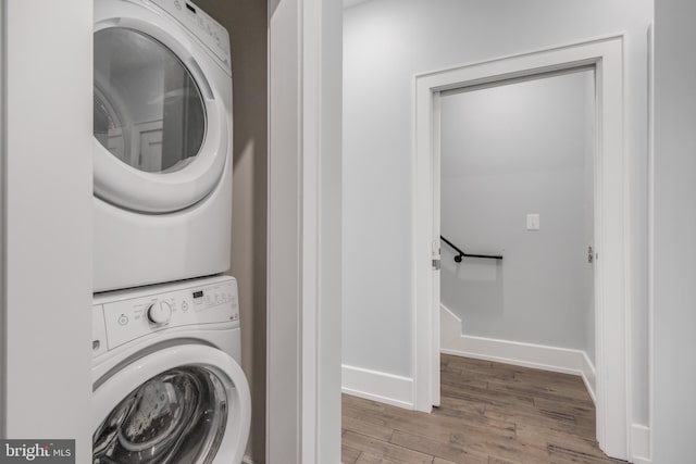 laundry room with laundry area, stacked washing maching and dryer, baseboards, and wood finished floors