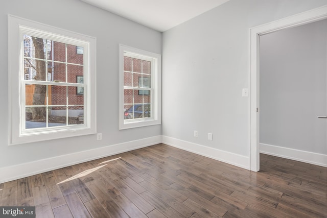 empty room with dark wood-style floors, plenty of natural light, and baseboards