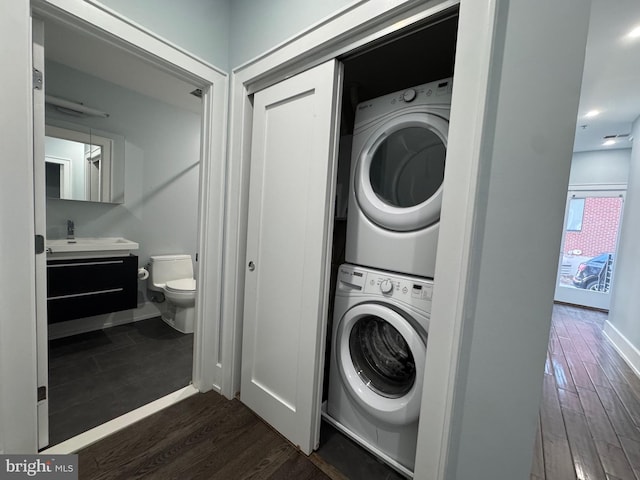 laundry area with baseboards, dark wood-style floors, laundry area, and stacked washer / dryer