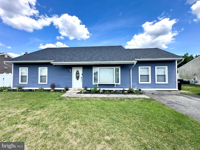 ranch-style house with a front yard, fence, driveway, and a shingled roof