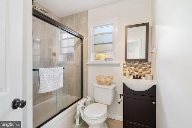 bathroom featuring toilet, enclosed tub / shower combo, tasteful backsplash, baseboards, and vanity