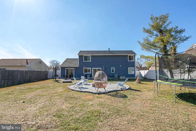 rear view of property with a trampoline, a fenced backyard, a yard, a fire pit, and a patio area