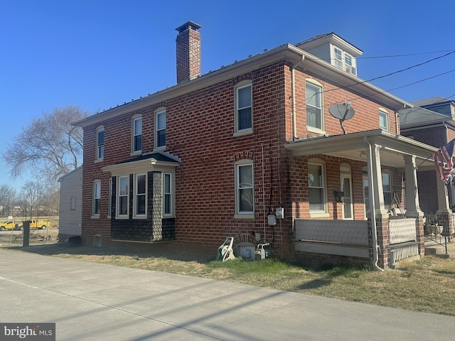 view of home's exterior featuring brick siding, a porch, and a chimney