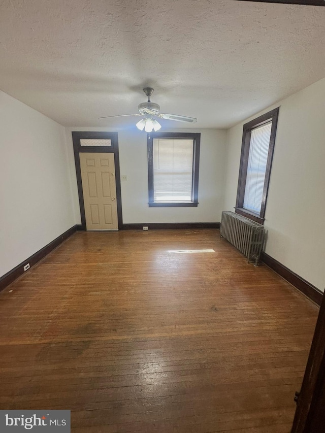 spare room with baseboards, radiator, wood finished floors, and a textured ceiling