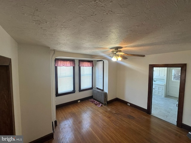 empty room featuring baseboards, radiator heating unit, ceiling fan, dark wood-type flooring, and a textured ceiling