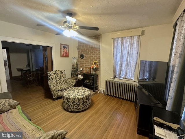 living room with a wood stove, a ceiling fan, wood finished floors, and radiator heating unit