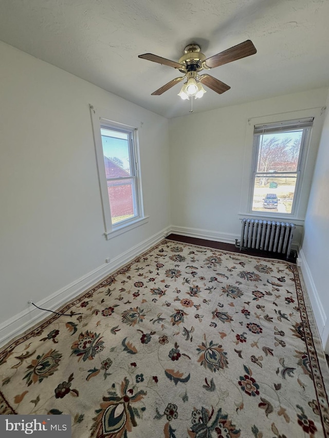 unfurnished room with baseboards, radiator, and ceiling fan