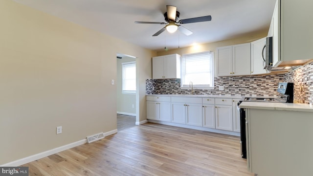 kitchen with electric range, light wood finished floors, visible vents, and backsplash