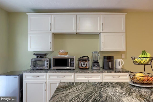 kitchen featuring stainless steel microwave, white cabinets, dark stone countertops, and refrigerator