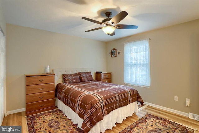 bedroom with a ceiling fan, wood finished floors, visible vents, and baseboards