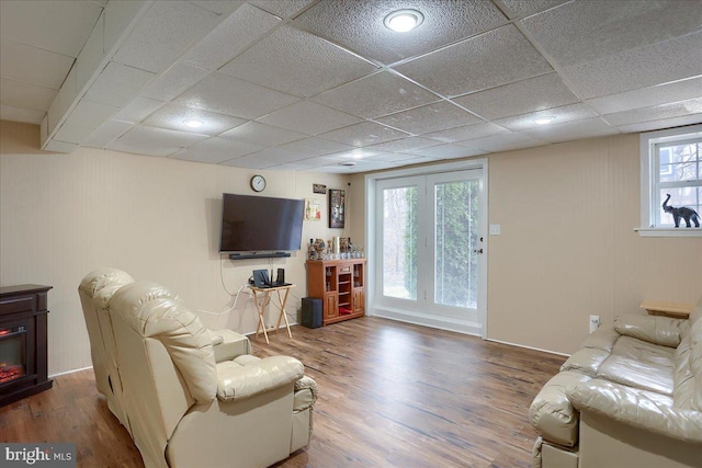 living area featuring a glass covered fireplace, a paneled ceiling, and wood finished floors