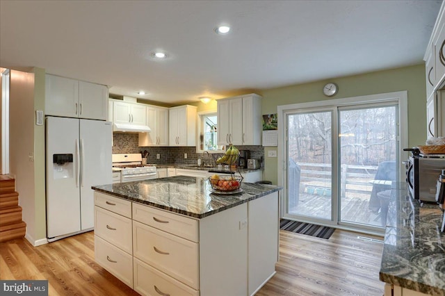 kitchen featuring white appliances, a sink, under cabinet range hood, light wood-type flooring, and backsplash