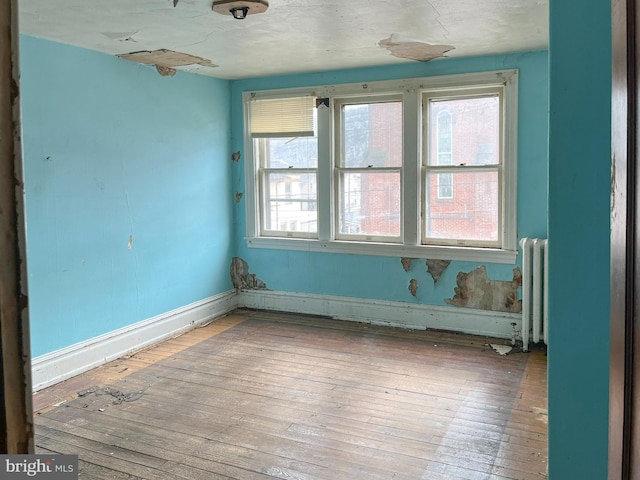 empty room with radiator heating unit, baseboards, and hardwood / wood-style floors