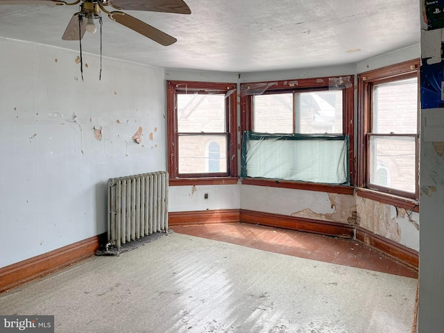 unfurnished room featuring a wealth of natural light, baseboards, a textured ceiling, and radiator heating unit