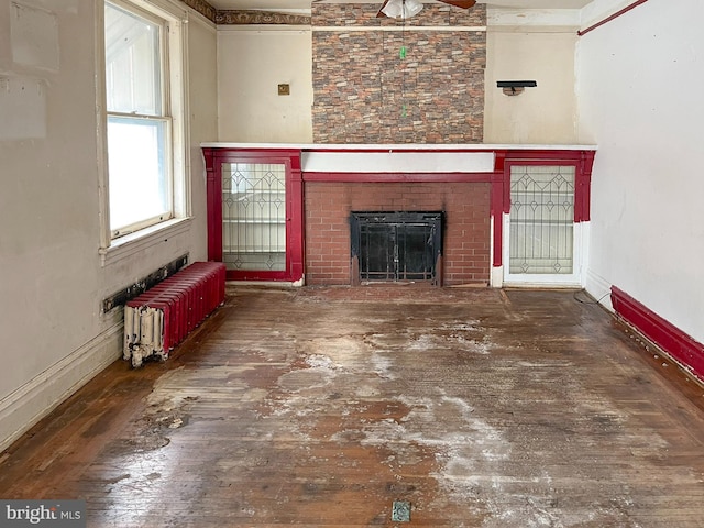 unfurnished living room with radiator, a fireplace, baseboards, and wood finished floors