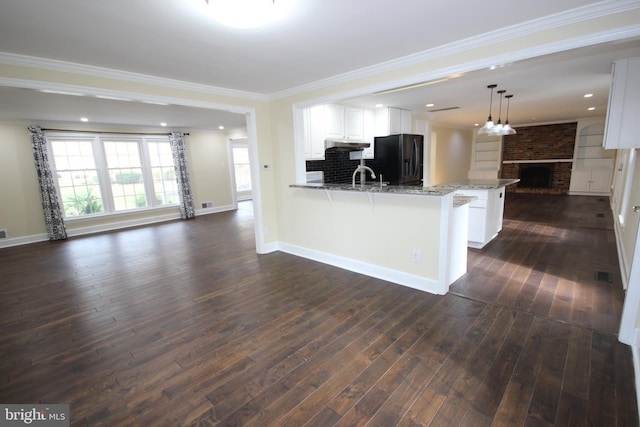 kitchen with black fridge, dark wood-style floors, open floor plan, a peninsula, and a fireplace