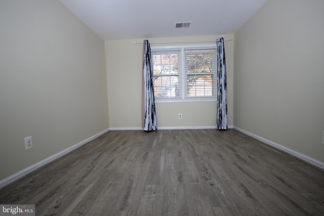 empty room featuring wood finished floors, visible vents, and baseboards